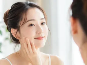 Close-up of a woman gently touching her cheek while looking in the mirror, preparing a skincare routine.