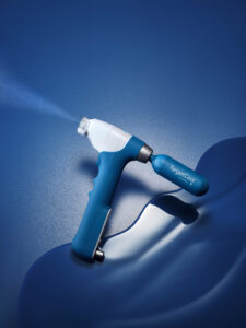 Close-up of a blue and white TargetCool handheld device spraying a fine mist on a blue surface.