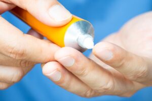 Close-up of hands squeezing white paste from an orange tube onto a fingertip.