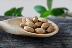 Pile of brown speckled tablets on a wooden spoon resting on a weathered surface.
