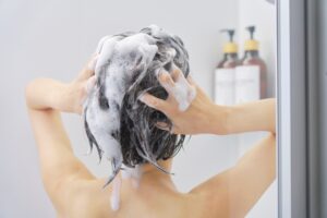 Person washing their hair in the shower, lathering shampoo through wet dark hair.