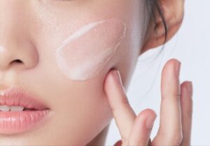 Close-up of a woman applying a white cream to her cheek with two fingers.